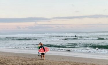 a couple of people walk on the beach carrying surfboards